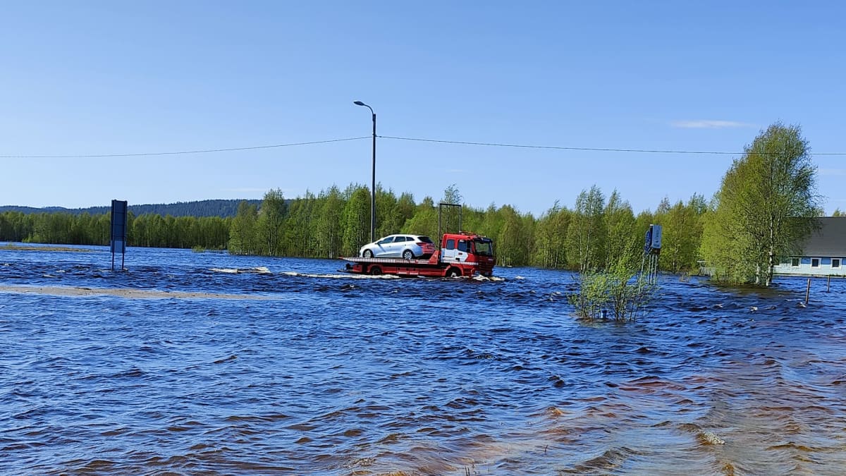 A tow truck carring a car through flood waters.