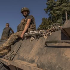 Ukrainian soldiers sitting on a tank, beneath a clear blue sky.