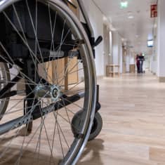 Fysioterapeutti avustaa vanhusta kävelyharjoituksessa Myyrmäen vanhustenkeskuksessa. Etualalla kuvassa pyörätuoli.