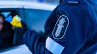 En person i polisuniform utför blåstest för alkohol på en person som syns suddigt i bakgrunden.