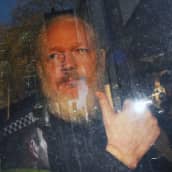 Julian Assange näyttää peukaloa auton ikkunasta.