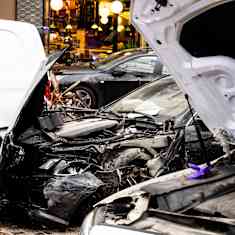 The front end of a smashed up car on a cobblestone street.