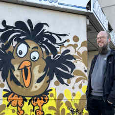 Savonlinnalainen graffitiharrastaja Toni Korhola hymyilee maalaamansa lintugraffitin luona Kauppalinnan edustalla.
