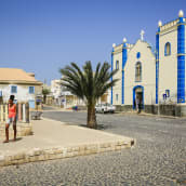 Kylän keskusaukio, jolla on kirkko, mukulakivikadut ja palmupuu.