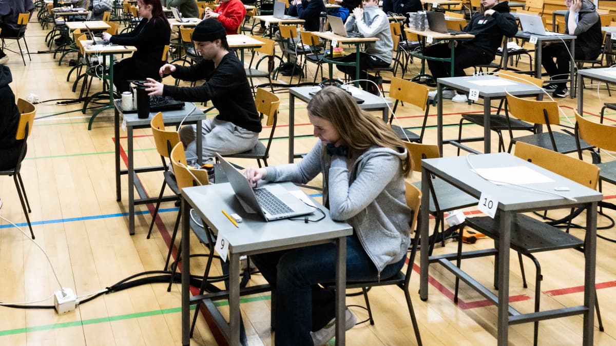 Nuoret istuvat riveissä yksittäisten pöytien ääressä läppärit edessään ylioppilaskirjoituksissa.