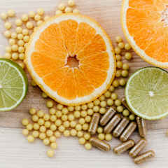 En halv apelsin och en halv lime på en träyta tillsammans med flera små, gula piller och några kapslar.