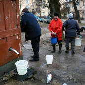 Ihmiset hakevat ämpäreihin vettä puistossa sijaitsevasta kaivosta.