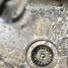 Vettä suihkuaa hanasta keittiön teräksiseen tiskialtaaseen.