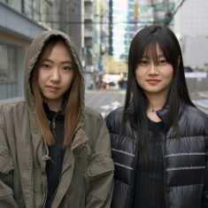 Kaksi nuorta korealaisnaista poseeraa kameralle kadulla.