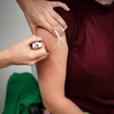 Hoitaja pistää rokotusta olkavarteen.