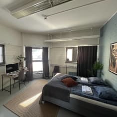 Kuvassa hotellihuone, jossa sänky, pöytä ja tuoli. Huoneessa on viisi ikkunaa. 