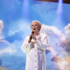 Katri Helena laulaa, taustalla sininen taivas missä pilviä. 