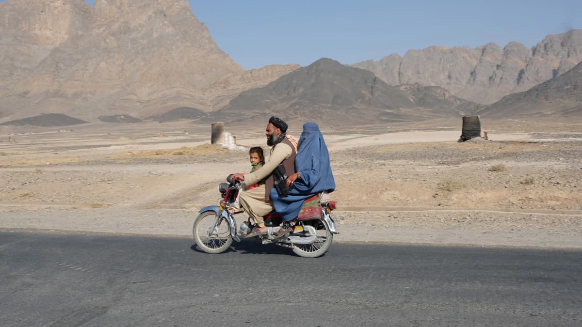 Mies kuljettaa moottoripyörän selässä siniseen burkaan pukeutunutta naista ja pientä lasta. 