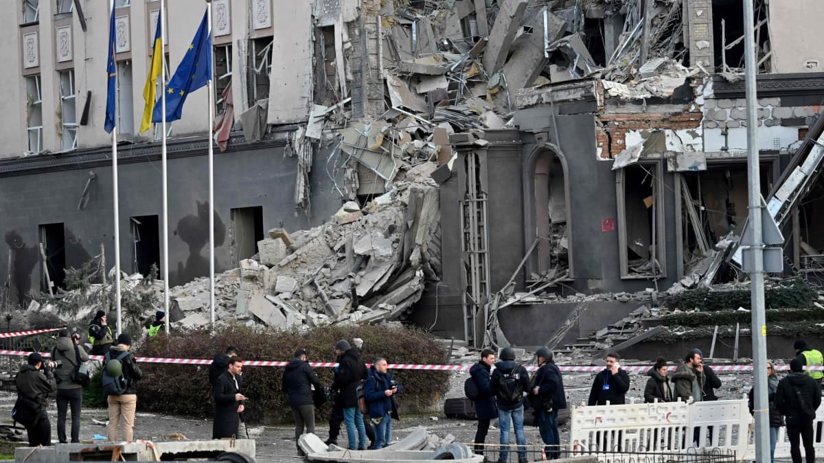 Osittain pommituksessa sortunut rakennus, jonka edessä seisoo ihmisiä.