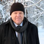Juha Joona mustassa takissa ja pipossa talvisessa maisemassa.