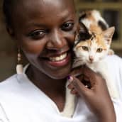 Nuori afrikkalainen nainen poseeraa hymyillen kissan kanssa. 