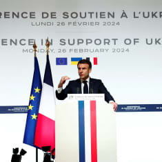Emmanuel Macron puhuu puhujankorokkella mikrofoniin. Vieressä Ranskan ja EU:n liput.