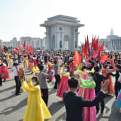 Ihmiset tanssivat torilla värikkäissä mekoissa ja tummissa puvuissa.