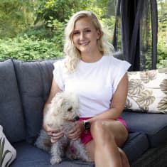 Essi Lundahl istuu ulkokatoksessa sohvalla vierellään pieni valkoinen koira.