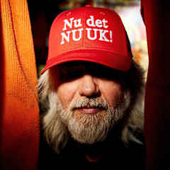 Mannen är klädd i en röd keps med texten "Nu det NU UK!" som är djupt neddragen över ögonen.