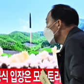 MIes kävelee ohjuksen laukaisua näyttävän television edessä.