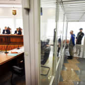 Sotarikoksista syytetty sotilas seisoo lasikopissa. Lasikopin ulkopuolella istuu tuomareita puisen pöydän takana.