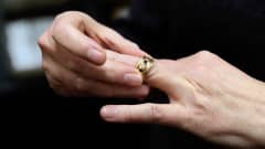 kulta sormus jossa on timantteja on ujutautumassa käteen sormeen joka on pikku rillin vieressä