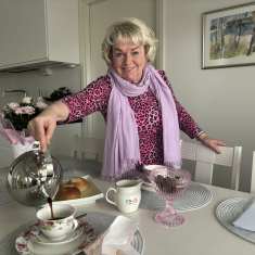 Hymyilevä nainen kaataa kuppiin kahvia keittiössä.