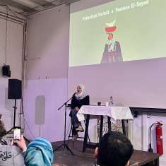 Hijab-päinen nainen puhuu mikkiin yleisön edessä. 