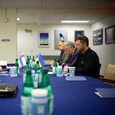 Half-dozen people, mostly in business attire, sitting on two sides of a table with small Finnish and Ukrainian flags. 