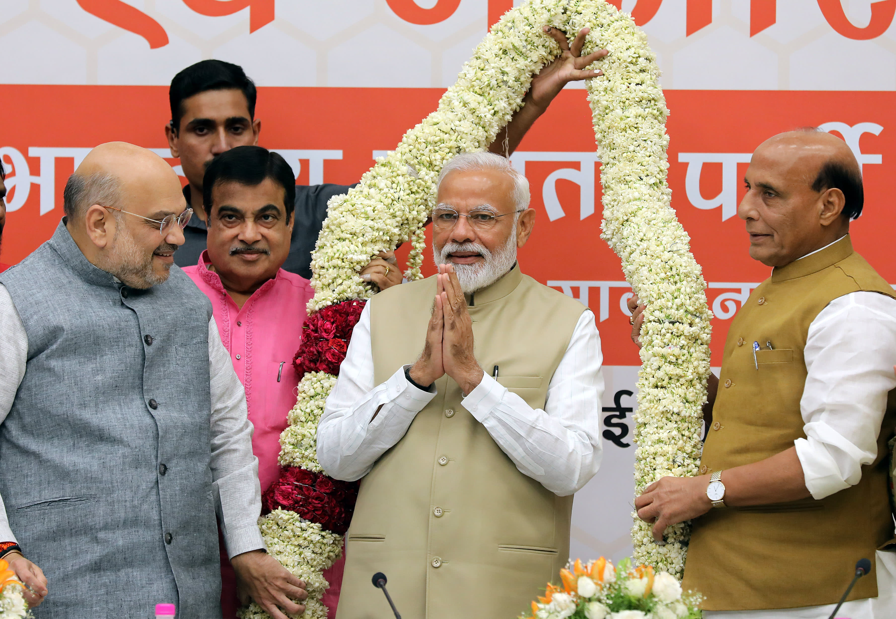 Pääministeri Narendra Modi seisoo puoluetovereidensa ympäröimänä. Taustalla suuri kukkaköynnös.