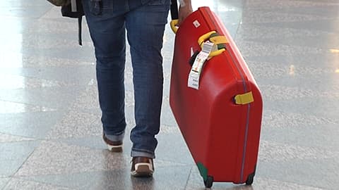 Matkustaja vetää perässään pyörillä kulkevaa matkalaukku lentokentällä.