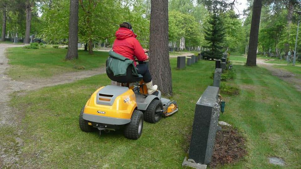 Kesätyöntekijä ajaa ruohoa hautausmaalla.