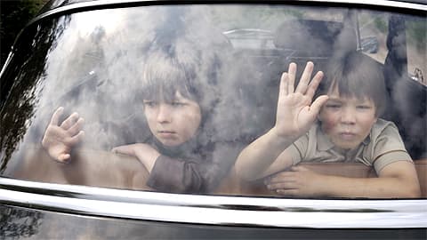 Kaksi pikkupoikaa painaa kätensä auton takaikkunaan. 
