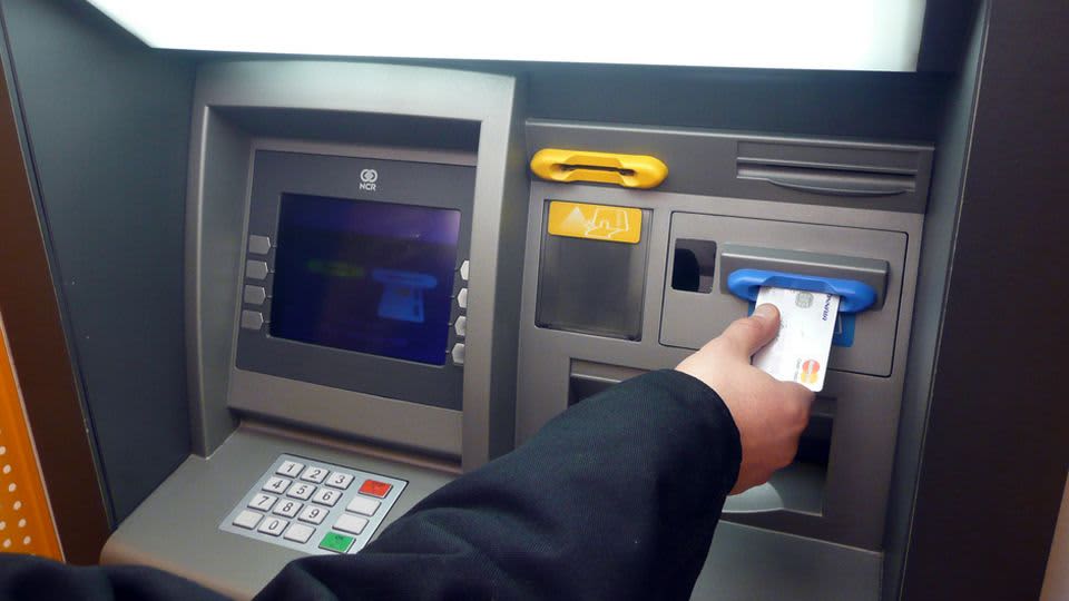 Käsi laittaa luottokorttia pankkiautomaatin siniseen kortinlukijaan.