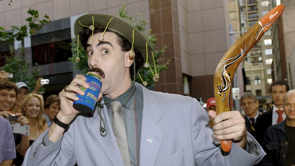 Borat juo olutta bumerangi kädessä