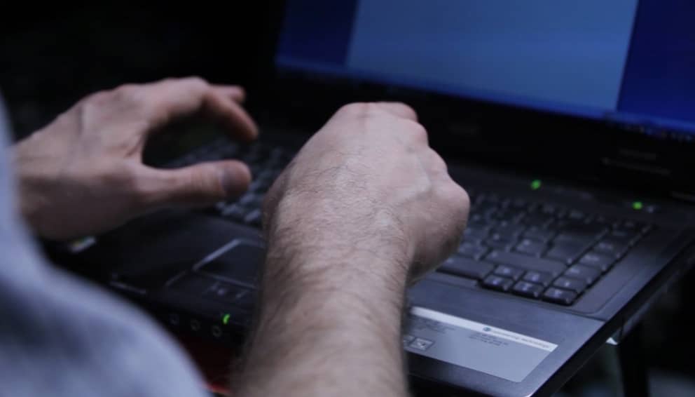 Mies kirjoittaa tietokoneella.