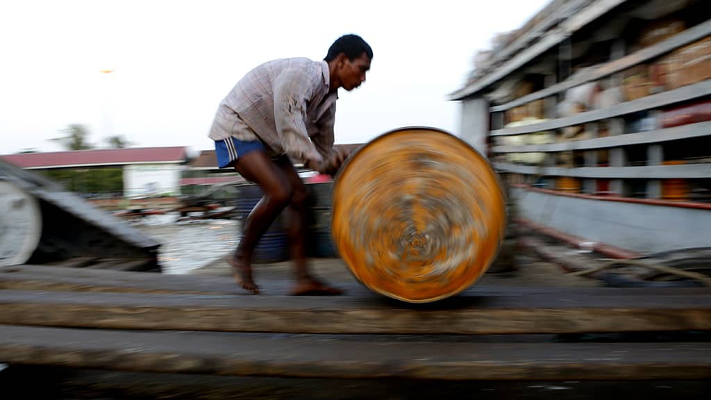 Työmies lastaa öljytynnyriä jokialukseen Yangossa, Myanmarissa.