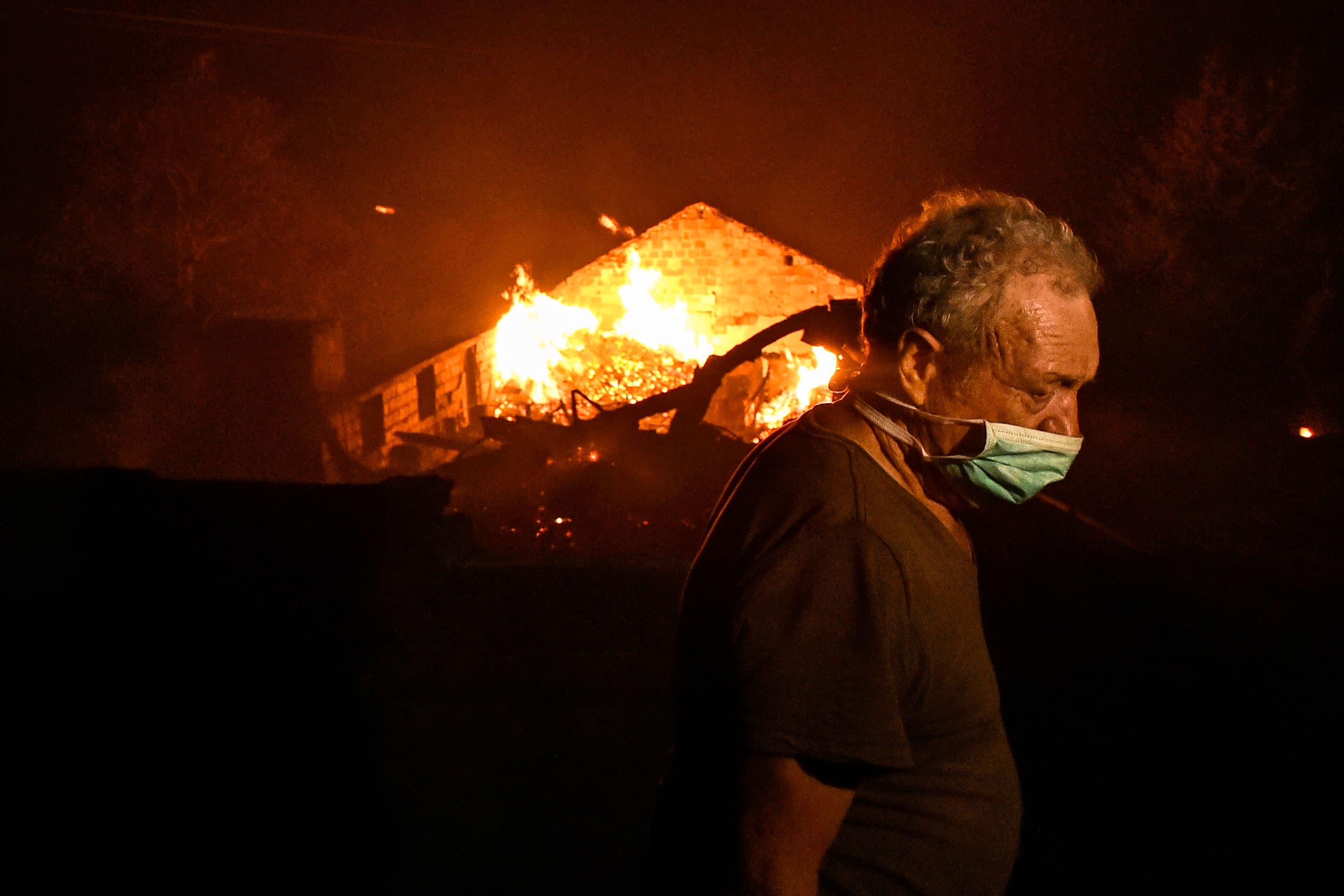 Mies hengityssuojaimen kanssa palavan talon edessä