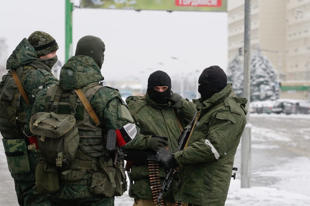 Neljä maastopukuista miestä kasvot peitettyinä ja aseet käsissään seisoo talvisella kadulla.