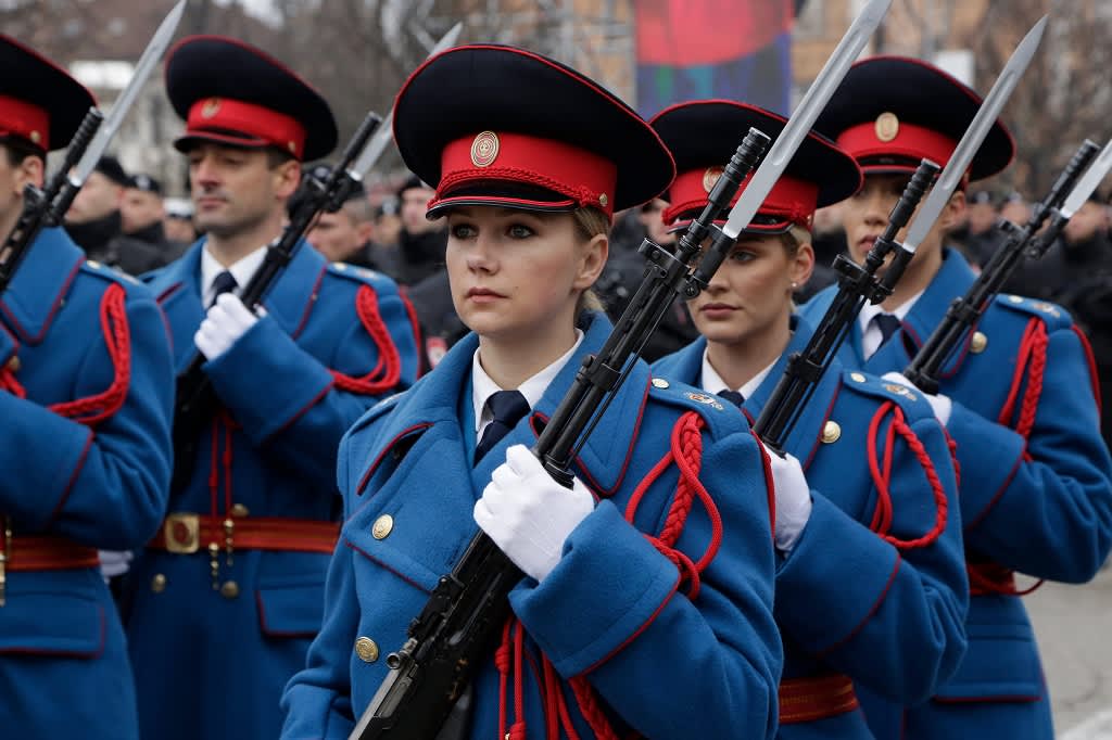 Kuvassa etualalla on naissotilas kivääri kädessään. Hänellä on sininen asu ja punamusta koppalakki päässään. Hänen lisäkseen kuvassa näkyy neljä muuta poliisivoimien sotilasta. 
