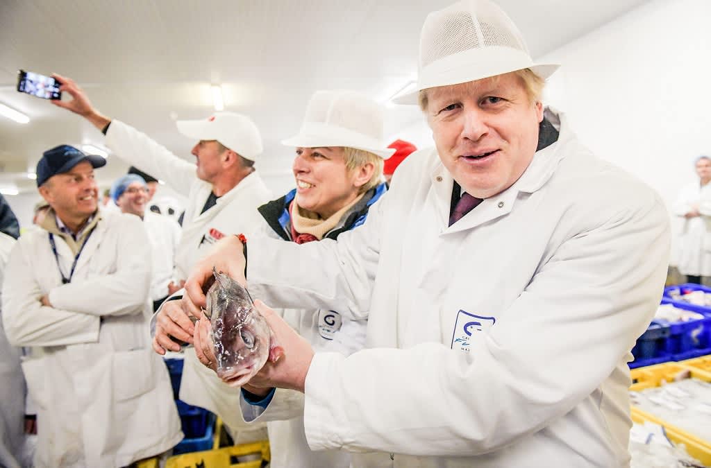 Kuvassa valko-asuinen Boris Johnson pitää käsissään kalaa. 