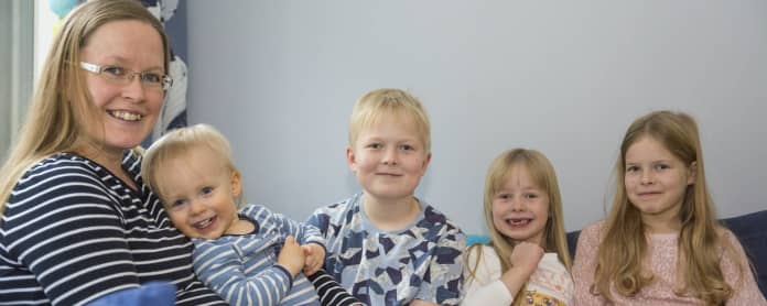 Viisihenkinen Heikkisten perhe kotisohvalla.