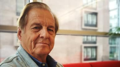 Tietokirjailija ja ulkomaankirjeenvaihtaja Rauli Virtanen istuu punaisella sohvalla.