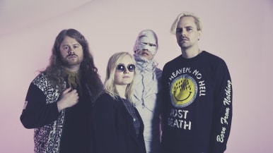 Ruusut-yhtye vaaleanpunaisen taustan edessä.