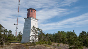 Mannen räddades i närheten av Orrengrunds fyr. En fyr med vit bas och röd topp står på ett berg. Runtomkring finns tallar.