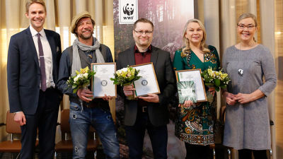 Antti Reini (andra från vänster) poserar med diplom och blombukett tillsammans med fyra andra personer. I bakgrunden syns en WWF-plansh.