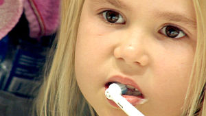 Pieni tyttö pesee hampaitaan sähköhammasharjalla.