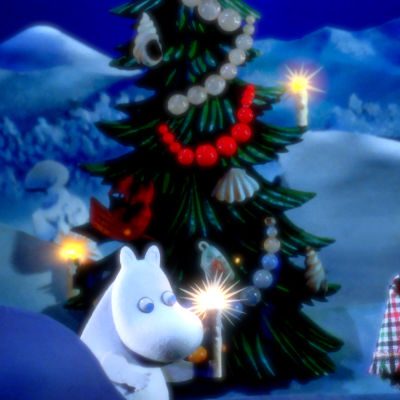 Mumintrollet står ute vid en pyntad julgran och håller i ett ljus, bredvid står hans föräldrar insvepta i en filt.