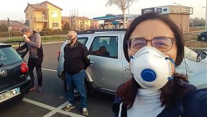 Chiara Di Marco berättar att priserna på masker och desinfektionsgel för händerna har stigit dramatiskt de senaste dagarna. En person i munskydd tar en selfie. I bakgrunden syns två andra med munskydd och bilar.